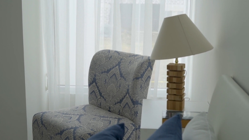 Mala i svetla spavaća soba sa elegantnom foteljom i stonom lampom pored kreveta