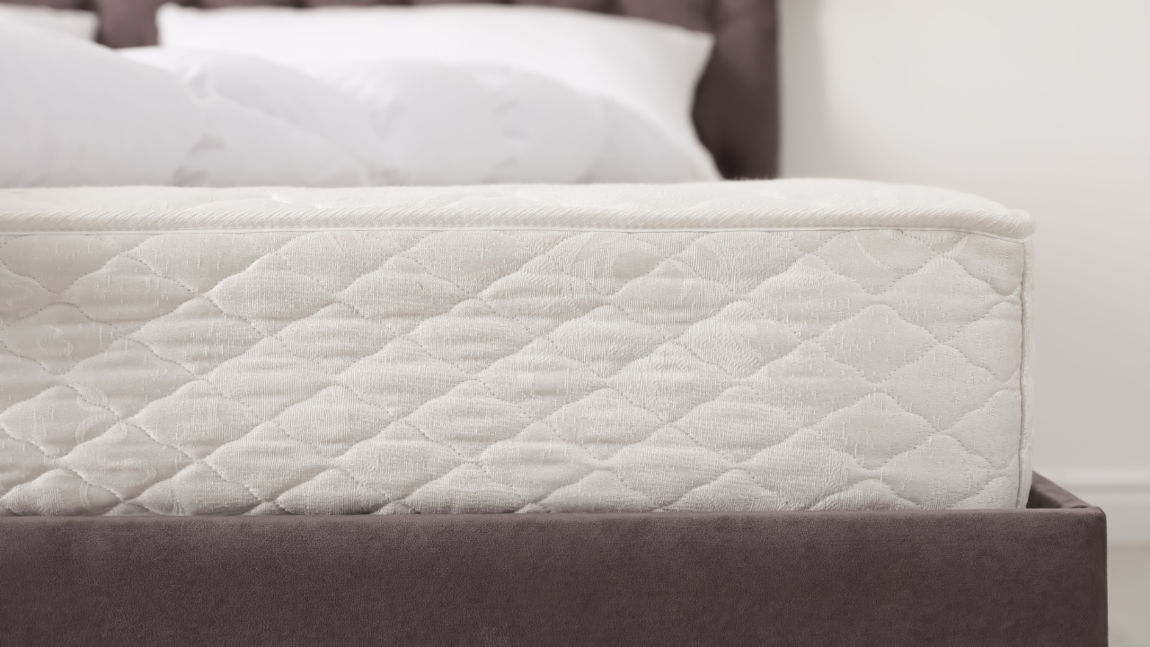 Krupan plan dušeka na bračnom krevetu sa prošivenom površinom i jastucima u pozadini